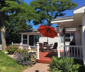 Une maison avec un porche abrité, une table à manger, des chaises et un parasol rouge.