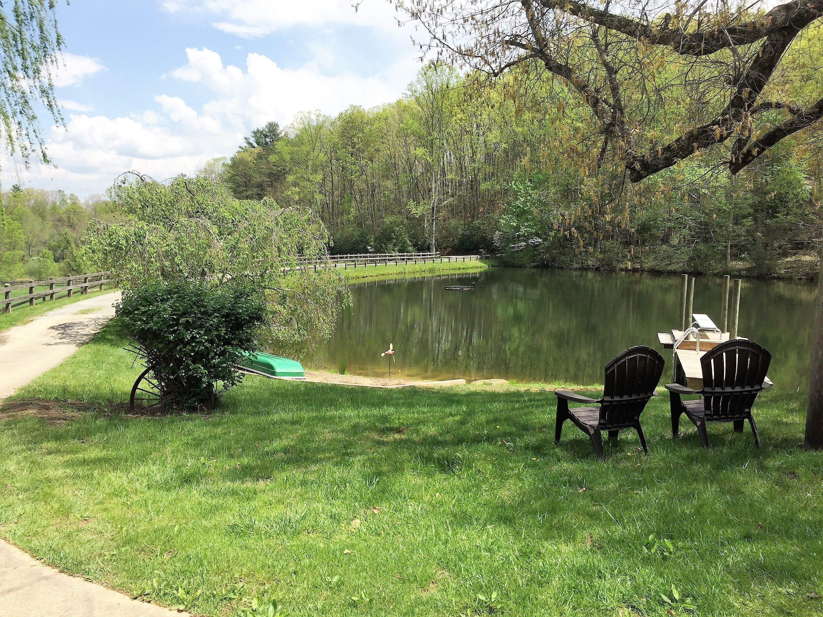A lakeside picnic area with a table and chairs, a green boat, and a wooden fence.