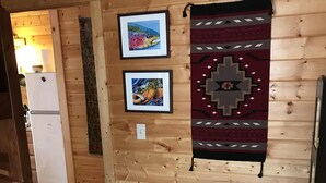 A cozy cabin interior with wooden walls, a bed with a colorful blanket, a small table with a water bottle, and two framed pictures on the wall. - Pristine Cabin near Craig...  Fish, or just Relax (Cascade)