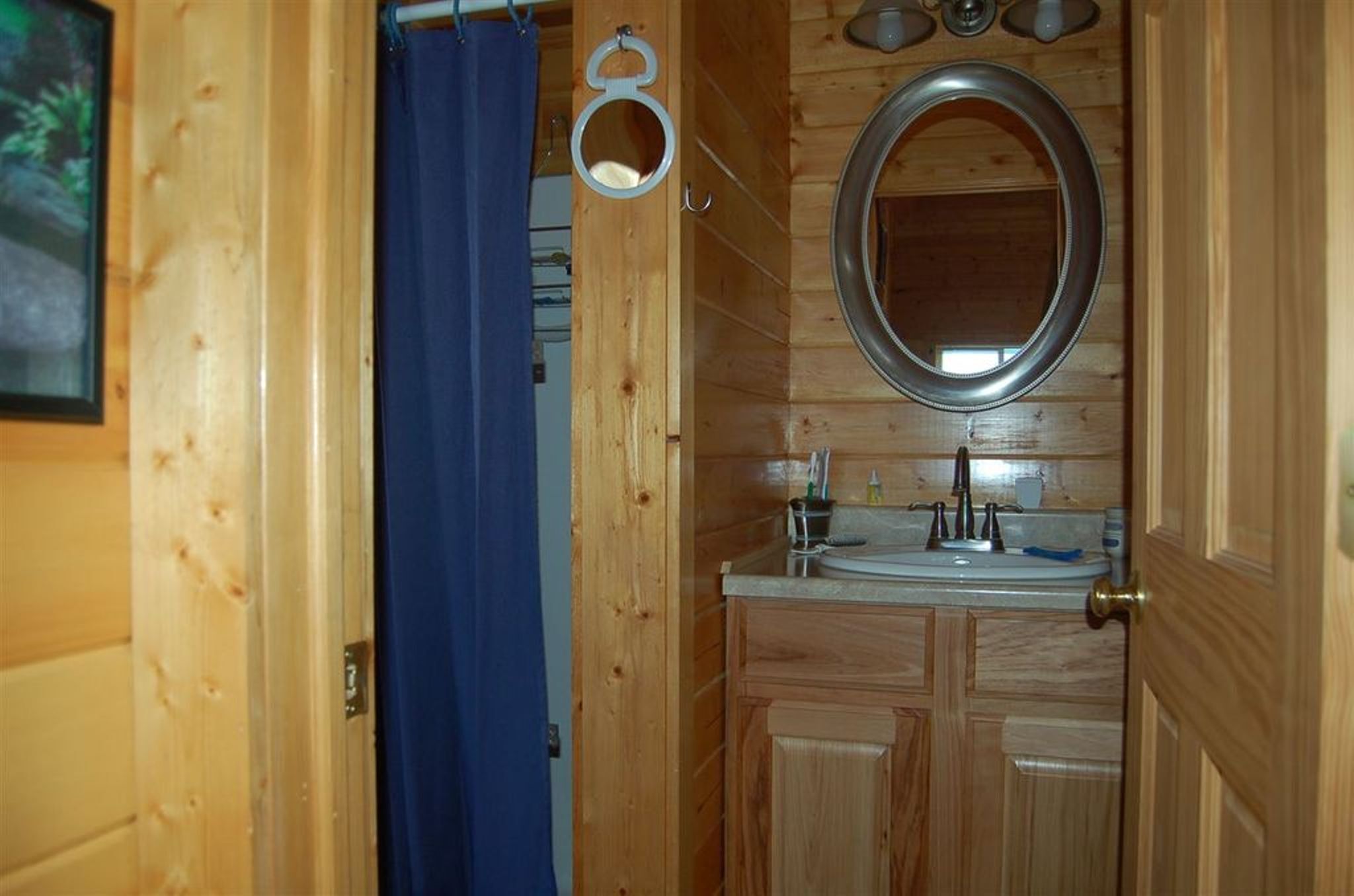 A wooden bathroom with a sink, mirror, and blue shower curtain.