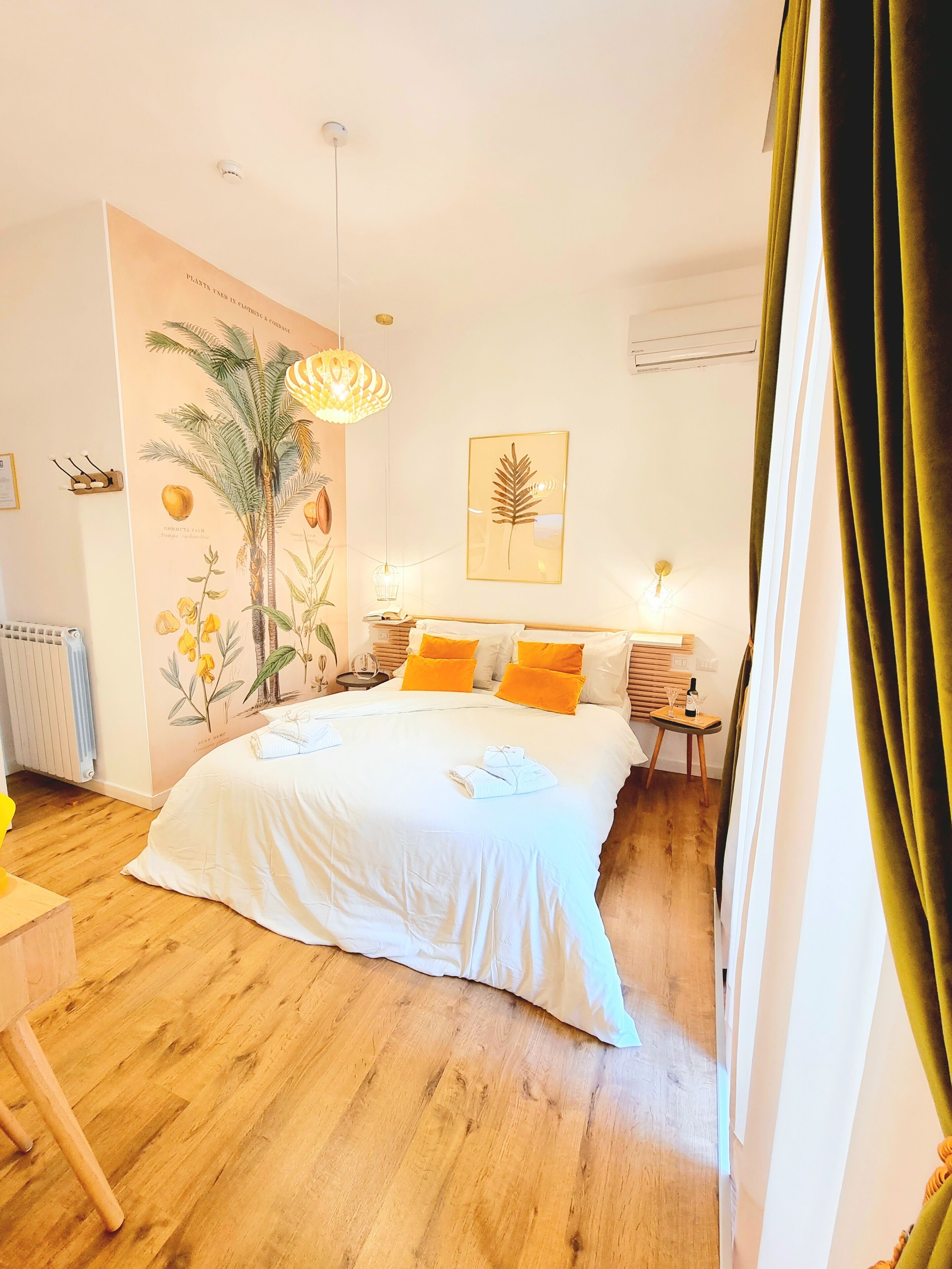 A bedroom with a large bed, a wall-mounted lamp, a radiator, and a small table with a bottle.