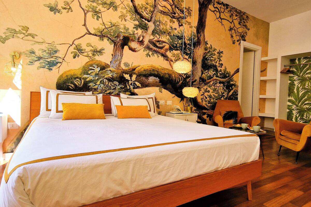Une chambre à coucher avec un grand lit, une table de chevet, une chaise, une lampe et une fresque murale.