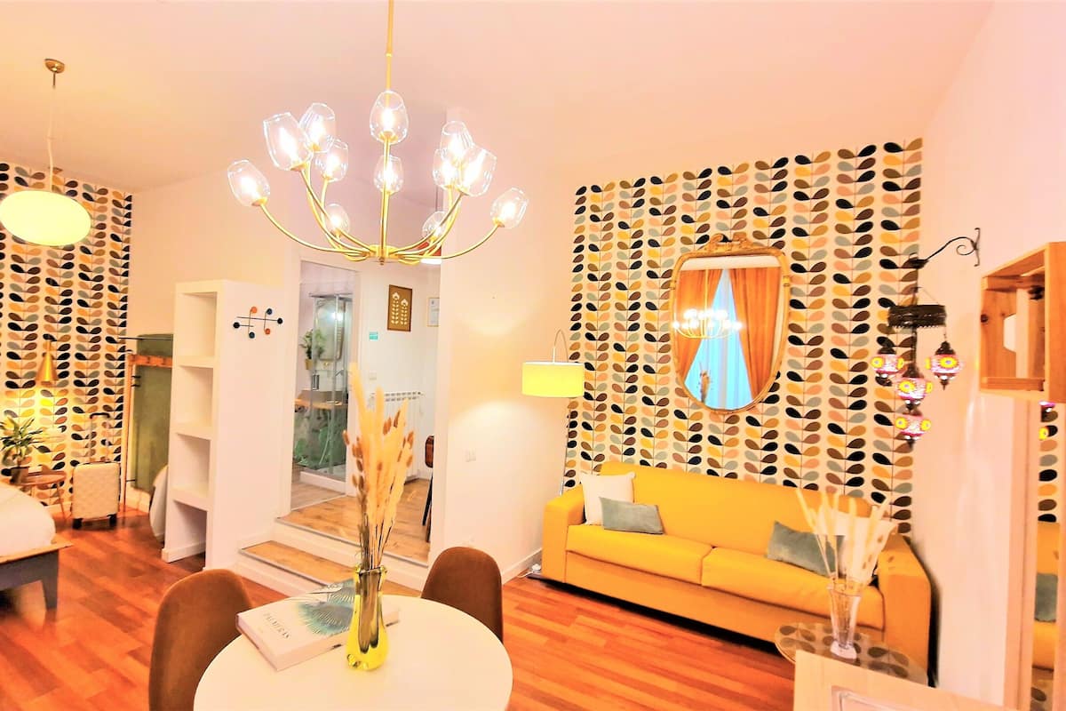 Un salon moderne agrémenté d’un lustre, d’un papier peint à motifs, d’un canapé et d’un coin repas avec une table et des chaises.