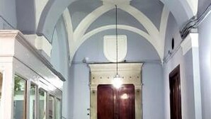 A hallway with a high ceiling and a central staircase leading to a dark door. - Napoli Tree - Lungomare (Naples)