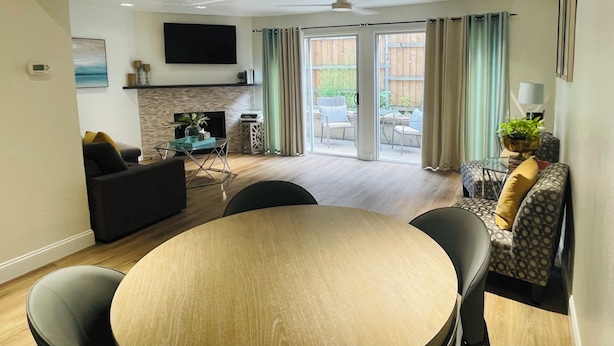 Een moderne woonkamer met een open haard, een eetgedeelte met een ronde tafel, en een groot raam met gordijnen.