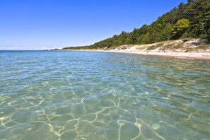 Ein Strand mit klarem, flachen Wasser, einem Sandstrand und einem bewaldeten Hügelhang.