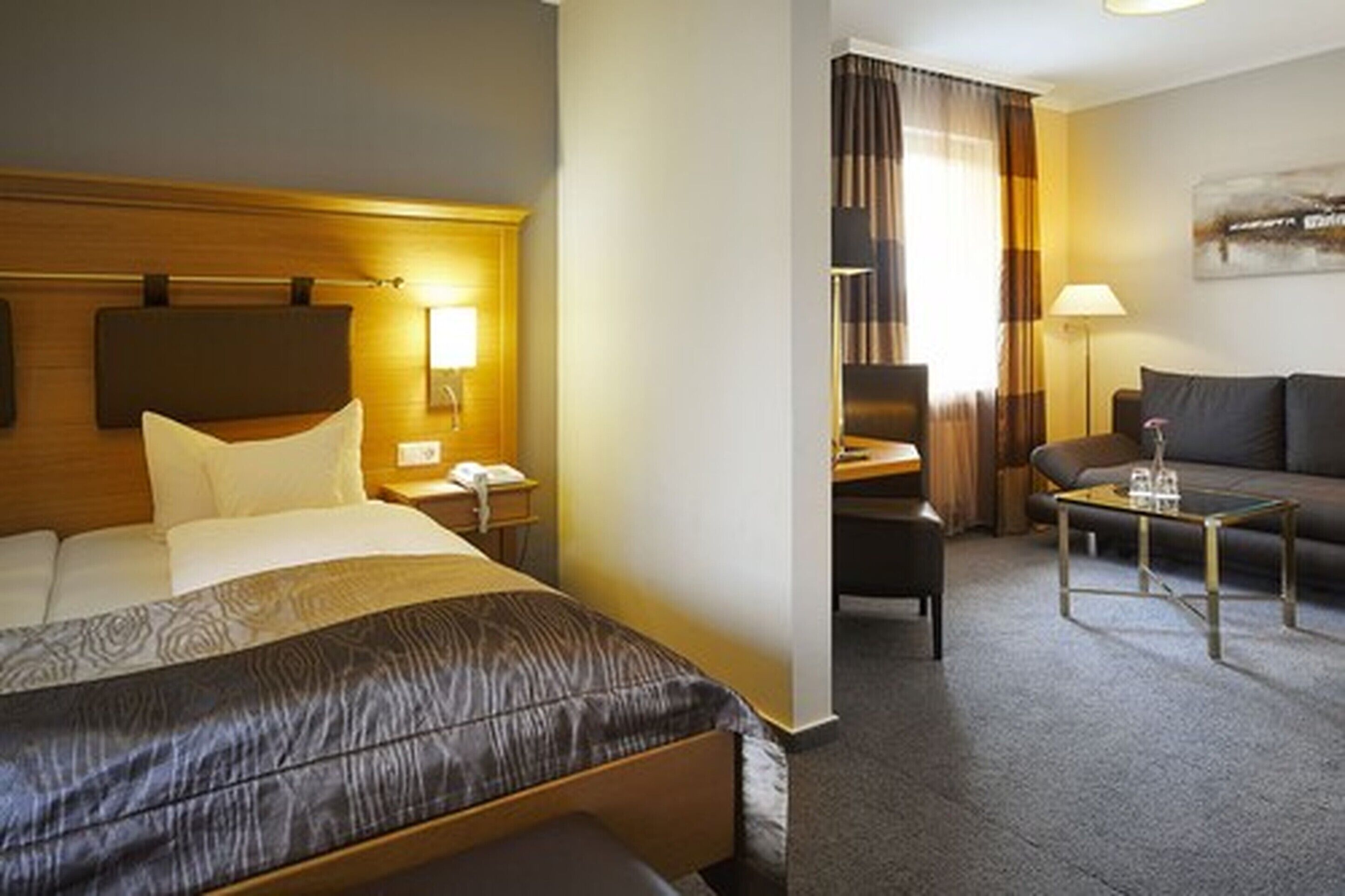 A hotel room with a bed, bedside table, lamp, and a sofa area with a coffee table.