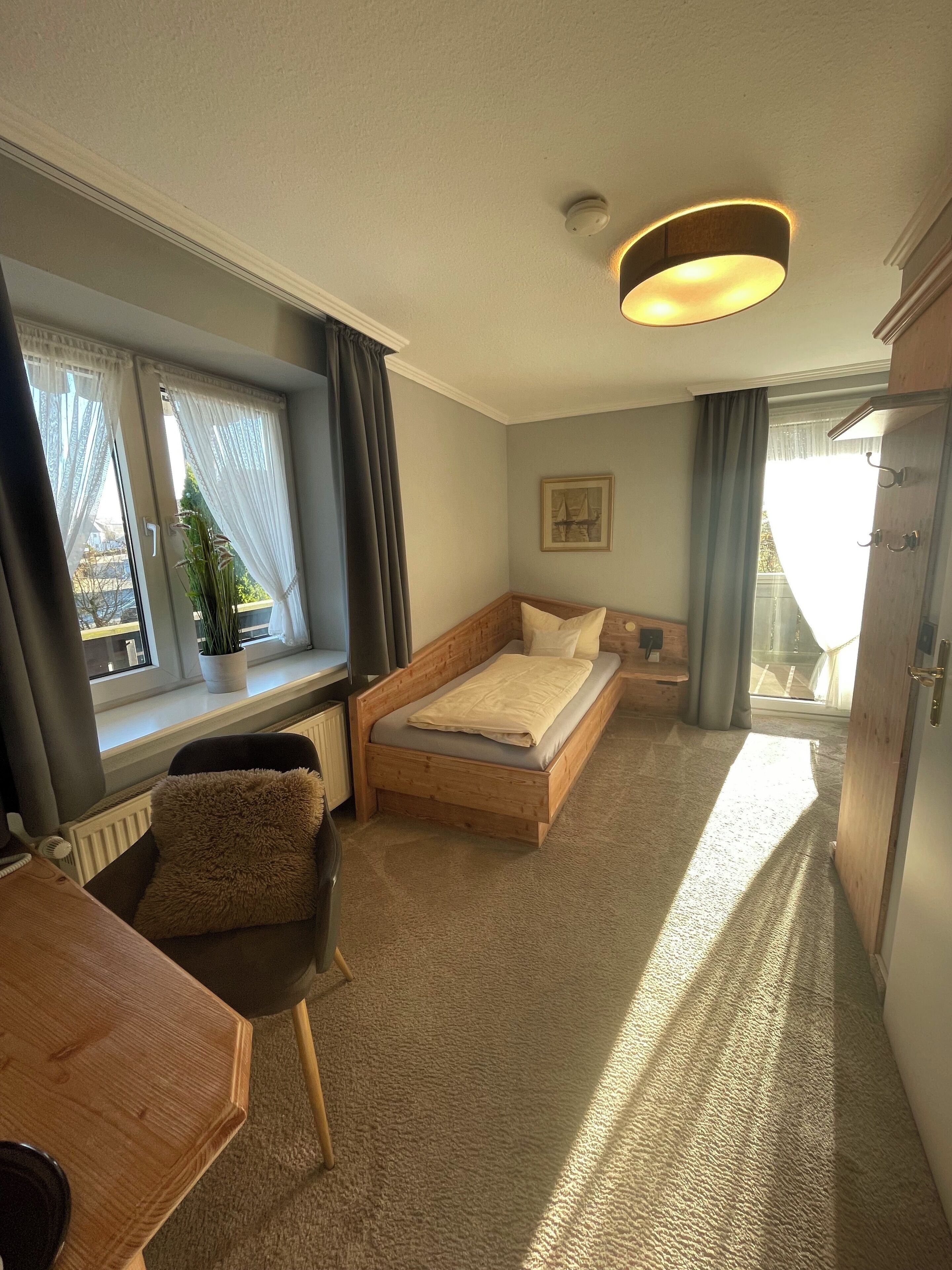 Une chambre à coucher de taille modeste, comprenant un lit, un petit bureau et une fenêtre avec des rideaux.