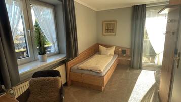 Een kleine slaapkamer met een bed, een bureau en een raam met gordijnen.