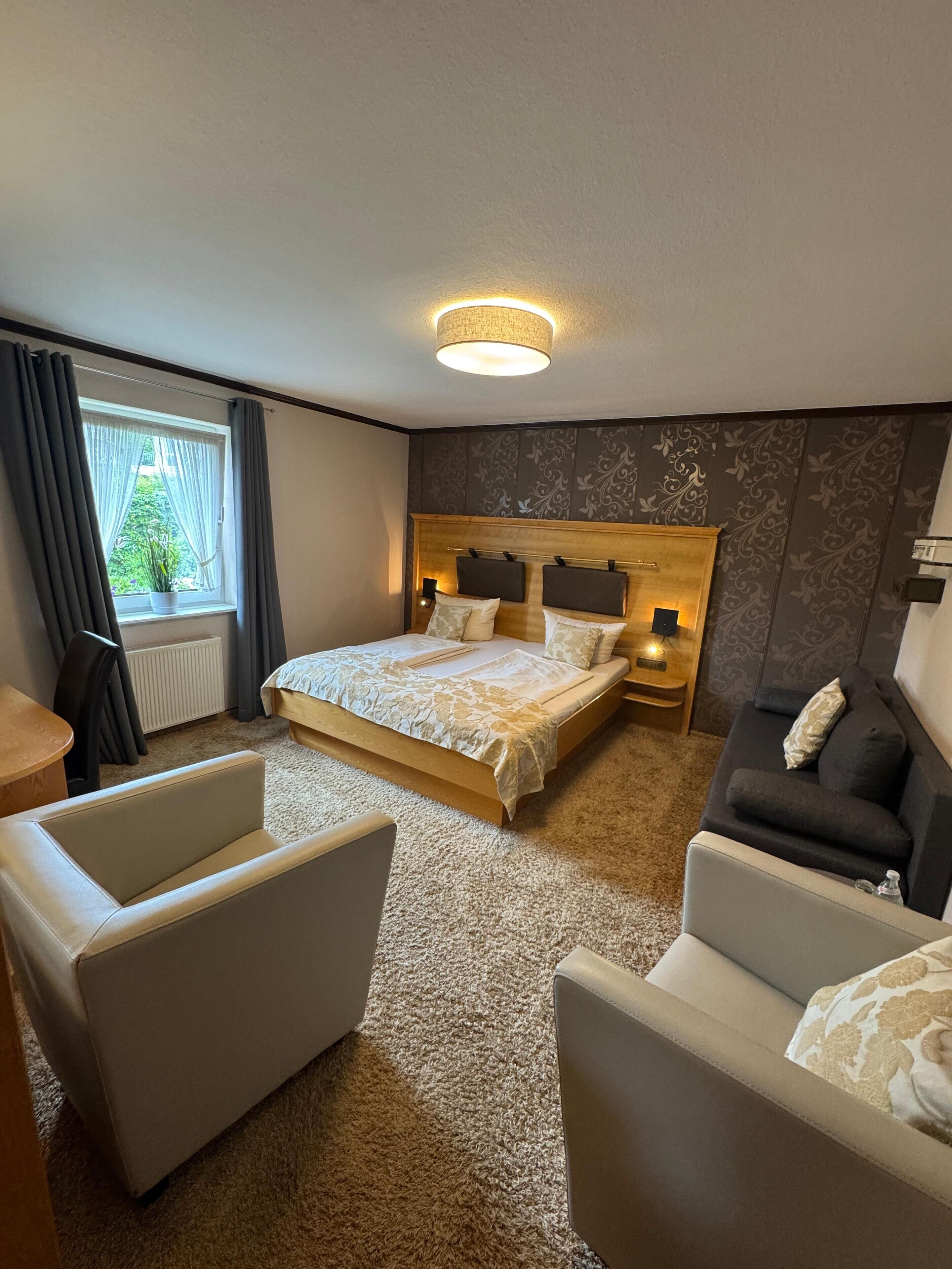 A hotel room with a large bed, two bedside tables, a sofa, and a chair.