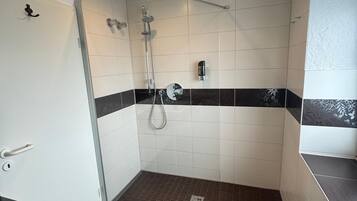 Ett modernt duschutrymme med en glasdörr, ett duschmunstycke som kan hållas i handen och en kontrollpanel.