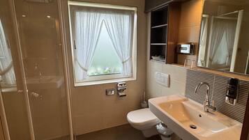 A modern bathroom with a glass-enclosed shower, a large sink with a mirror, and a window with curtains.