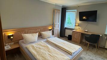Een hotelkamer met een bed, bedlampen, een bureau, een televisie en een raam met gordijnen.