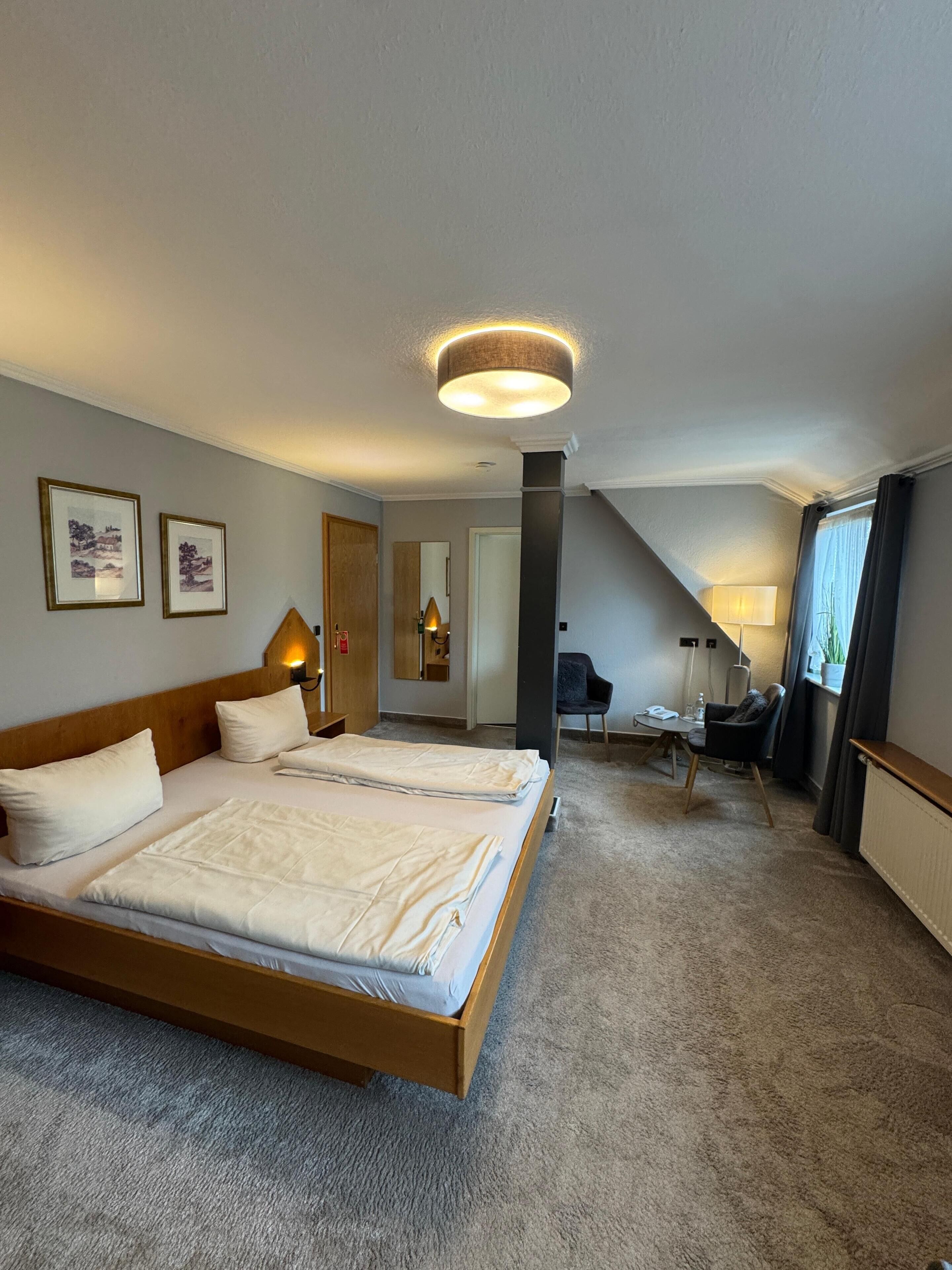 A hotel room with two beds, a desk, a chair, a lamp, and a ceiling light.