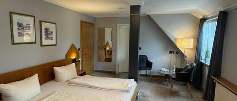 A hotel room with two beds, a desk, a chair, a lamp, and a ceiling light.