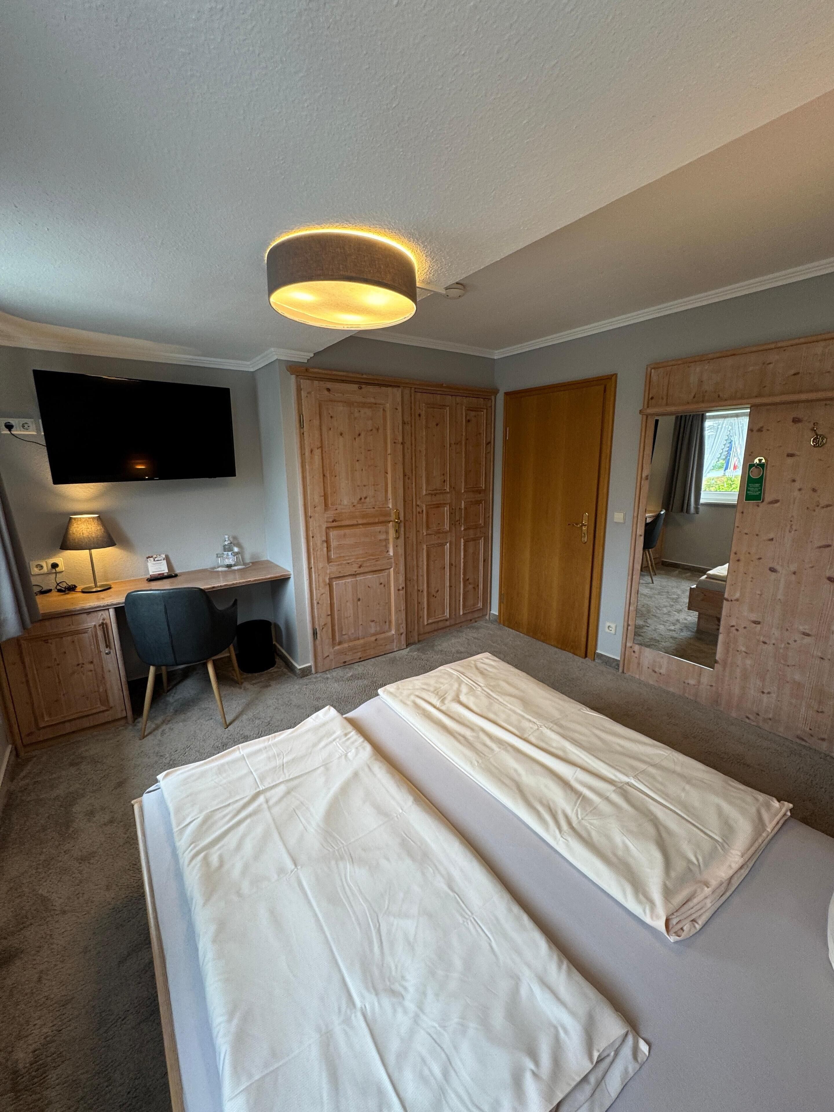 Quarto com duas camas, uma escrivaninha, uma cadeira, televisão e armários de madeira.