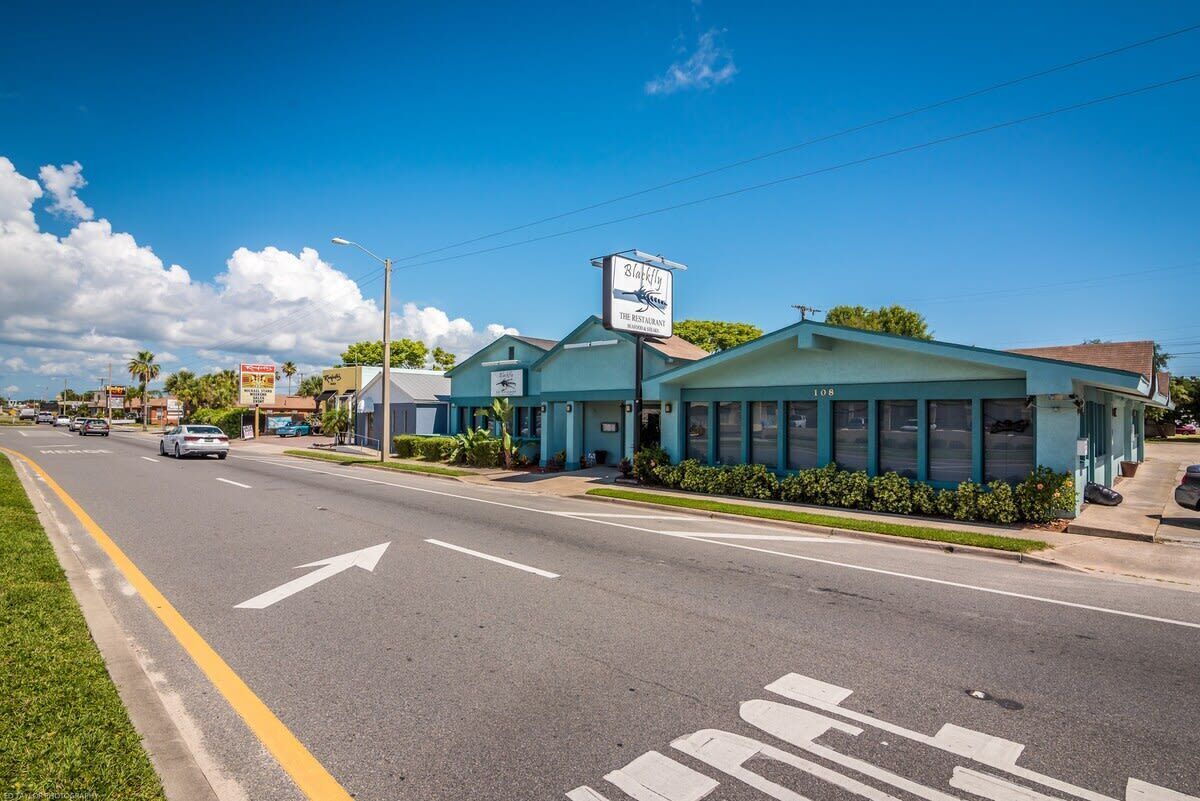 A restaurant with a signboard, a road with directional arrows, and a clear sky.