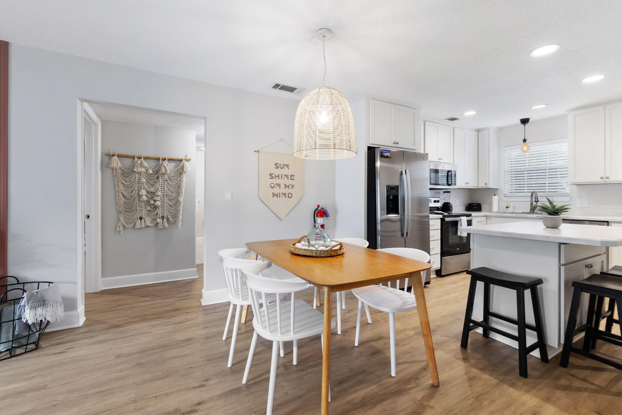 A modern kitchen with white cabinets, a wooden dining table, and a hanging light fixture.