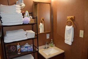 A bathroom with a sink, mirror, towel rack, and shelves with towels and toiletries. - Cabin In The Wildwood (Chehalis)