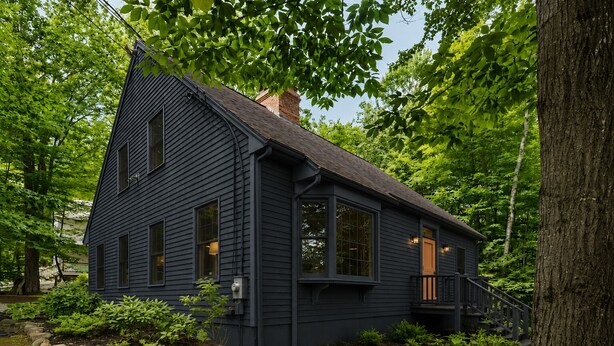 Una casa azul oscuro con un techo a dos aguas pronunciado, ventanas amplias y un porche delantero.