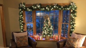 Una sala de estar acogedora con sillones de cuero, un árbol de Navidad y una ventana con vistas a la ciudad de noche.