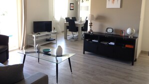 Ein Wohnzimmer mit Glastisch, Fernseher, Essbereich mit Stühlen, einem schwarzen Schubladenschrank und einem wandmontierten Globus.