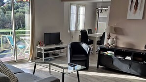 Ein modernes Wohnzimmer mit einer Couch, einem Glastisch, einem schwarzen Sessel, einem Fernseher und einem Essbereich mit Tisch und Stühlen.