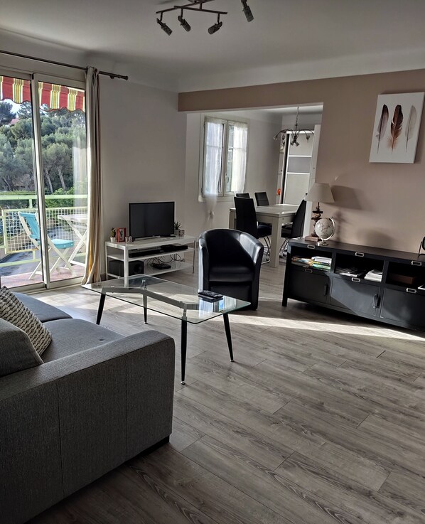 Una sala de estar moderna con un sofá, una mesa de centro de vidrio, un sillón negro, un televisor y una zona de comedor con una mesa y sillas.