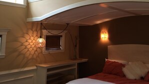 Ett sovrum med en säng i loftstil, ett skrivbord och en hängande lampa.