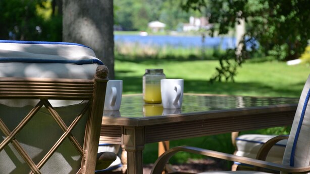 Ett bord med ett glas apelsinjuice, tv å vita muggar och en stol av rotting.