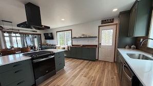 A modern kitchen with dark cabinets, a built-in oven, and a large window overlooking a lake. - Cottage on a Lake.  Near Pictured Rocks/ Munising (Manistique)