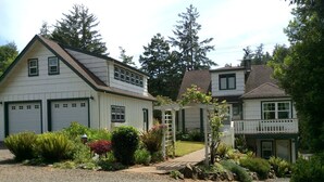 A two-story house with a gravel driveway and a garden with various plants and a wooden arbor. - NO CLEANING FEES! A Little Bit of Heaven-FREE Kayaks-Launch From Bank-Near Beach (Waldport)