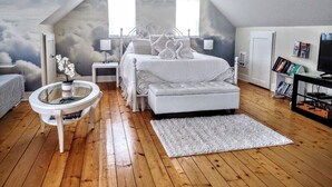 A bedroom with a sloped ceiling, a bed with a white headboard, a round glass table, a white rug, and a bookshelf. - NO CLEANING FEES! A Little Bit of Heaven-FREE Kayaks-Launch From Bank-Near Beach (Waldport)