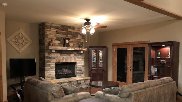 A living room with a stone fireplace, two sofas, a small round table, and a ceiling fan.