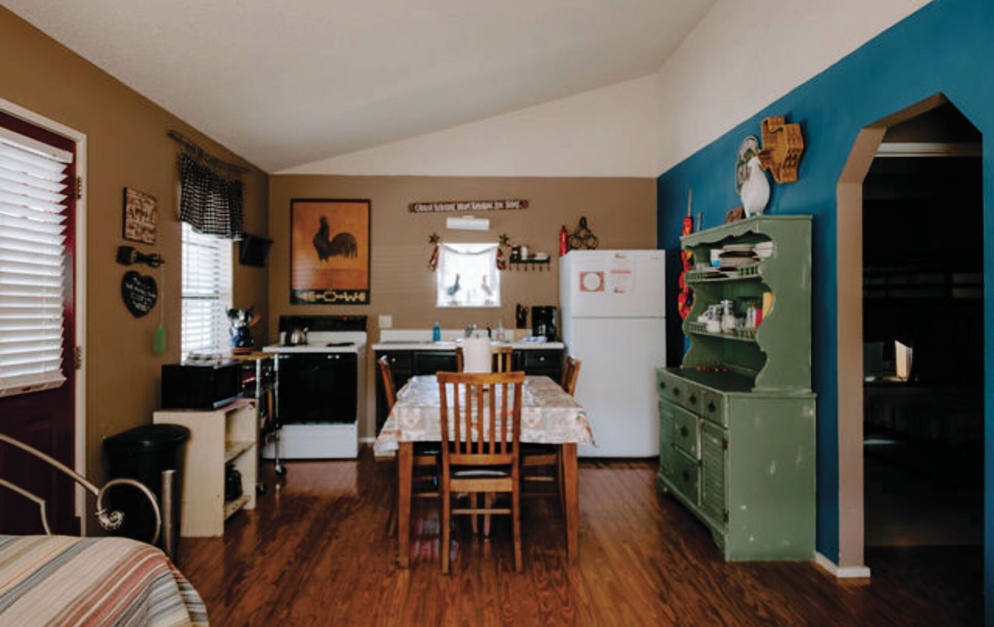 A compact kitchen with a dining table and chairs, a refrigerator, and a green cabinet.