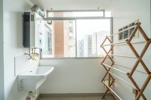 A small, bright bathroom with a window, a sink, and a wooden drying rack. - Ocean view apartment close to airport  (San Miguel)