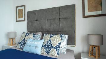 Une chambre à coucher avec une tête de lit capitonnée, des coussins à motifs, une couvre-lit bleue et des lampes de chevet posées sur des supports en bois.