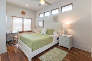 A bedroom with a bed, bedside tables, a desk, and a ceiling fan.