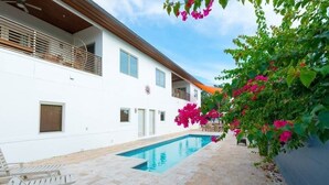 A modern building with a swimming pool, outdoor seating, and vibrant bougainvillea flowers.