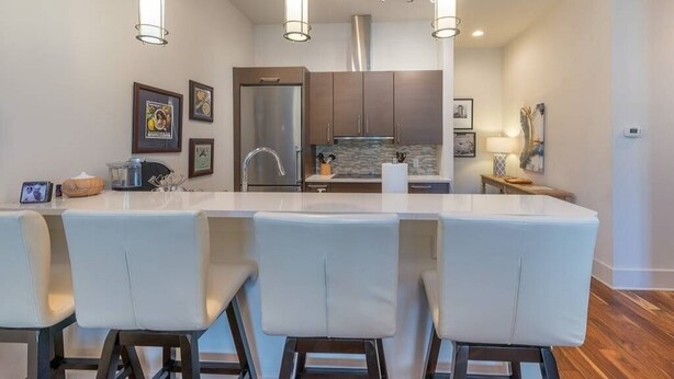 A modern kitchen with a central island, bar stools, stainless steel appliances, and pendant lighting.