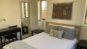 A bedroom with a bed, a desk, a chair, a nightstand, a lamp, and a window. - Contemporary Guest House--Close In, Great Views (Santa Fe)