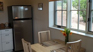 A compact kitchen with a refrigerator, a dining table with chairs, a window with a view of greenery, and a small painting on the wall. - Contemporary Guest House--Close In, Great Views (Santa Fe)