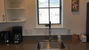 A kitchen with a stainless steel sink, white cabinets, a coffee maker, and a window with a view of a sandy area. - Contemporary Guest House--Close In, Great Views (Santa Fe)
