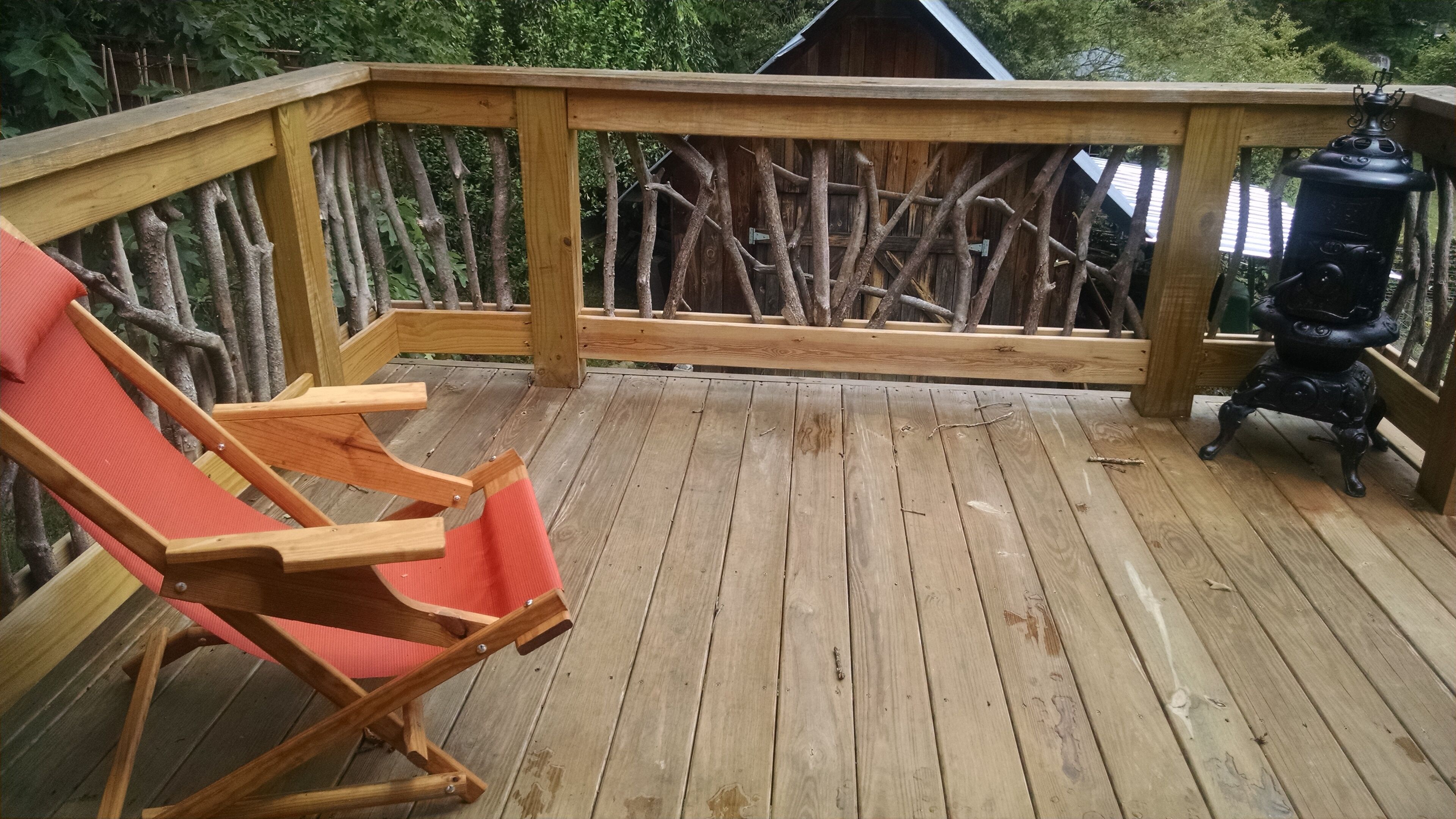 A wooden deck with a red lounge chair, a lantern, and a rustic fence.