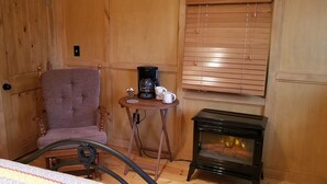 A cozy room with a wooden chair, a small table with a coffee maker, and a wood-burning stove.