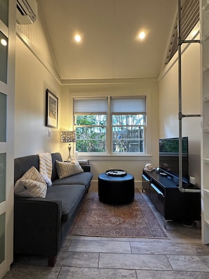 Una sala de estar con sofá, reposapiés y televisor sobre un mueble.