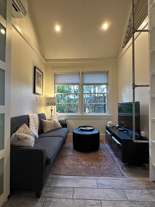 A living room with a sofa, ottoman, and a television on a stand.