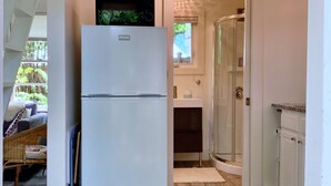 Una cocina compacta con un refrigerador blanco, una cabina de ducha de vidrio y una ventana pequeña.