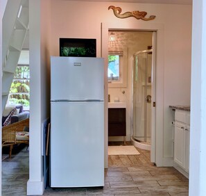 A compact kitchen with a white refrigerator, a glass shower enclosure, and a small window. - Unique Zen Tiny House 2 mi to Beach ~ Free Bikes! Minutes to Historic Charleston (Mount Pleasant)