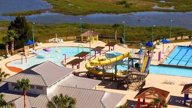 Vista aérea de un parque acuático con múltiples piscinas, toboganes y una piscina central grande.